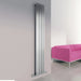 Carisa Sarp Vertical Stainless Steel Designer Radiator, in a living space next to a fuchsia pink sofa 