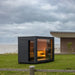 close up of the saunum classic sauna with ambient lights on with the sauna house within the garden of a modern house by the sea